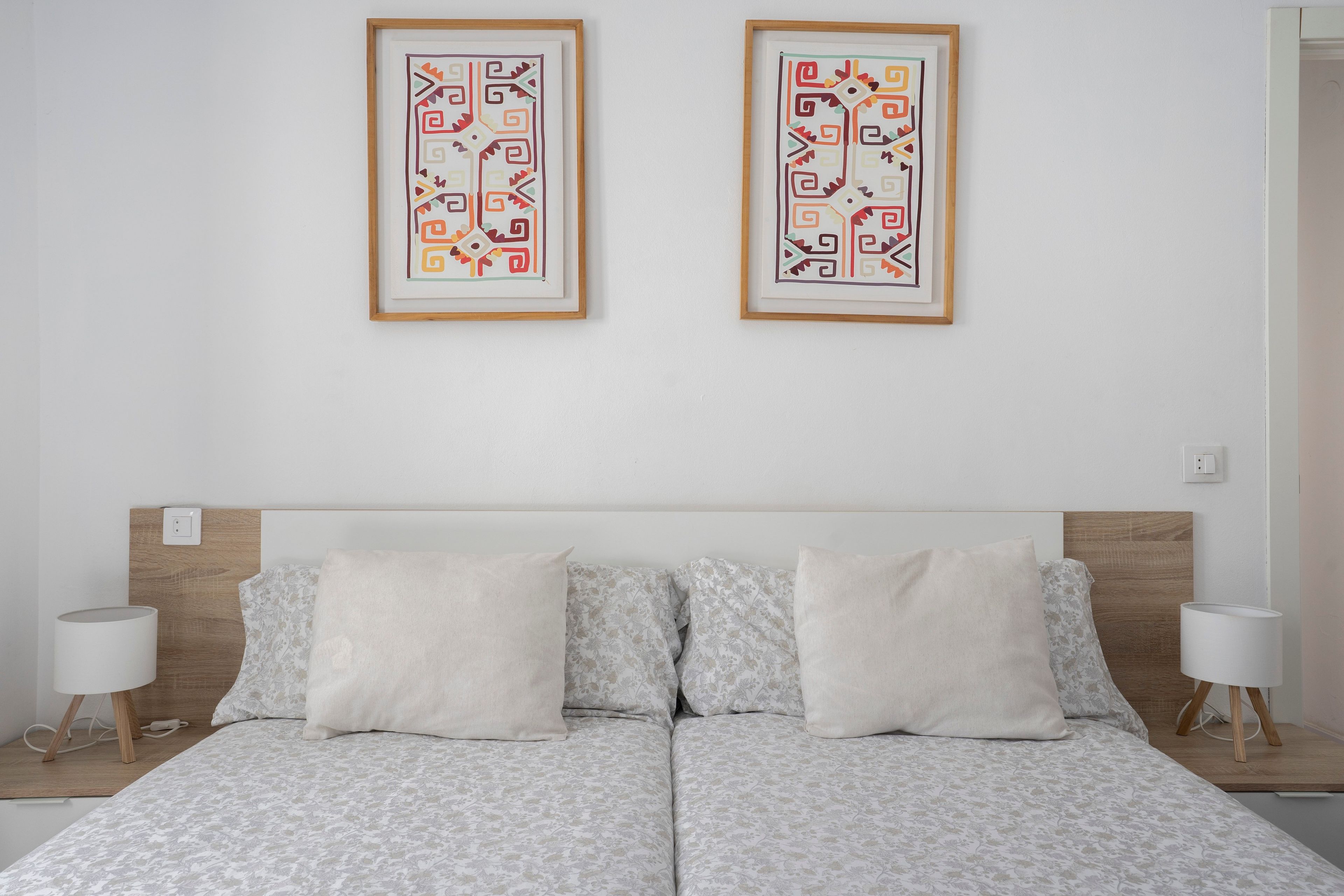 Una cama doble con colcha de estampado floral, dos almohadas blancas y un cabecero de madera.