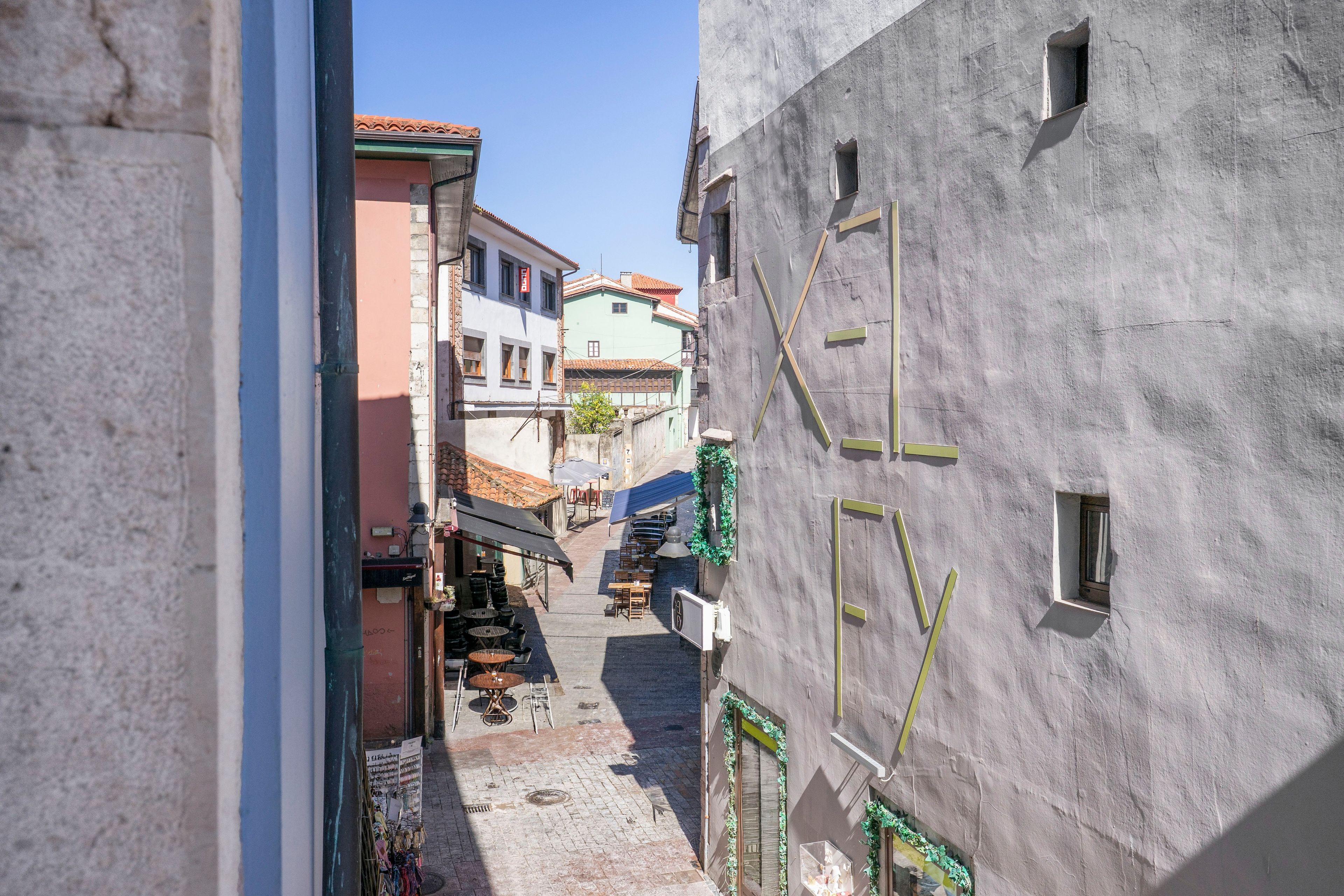 Una calle estrecha flanqueada por edificios, un camino empedrado y mesas de café al aire libre.