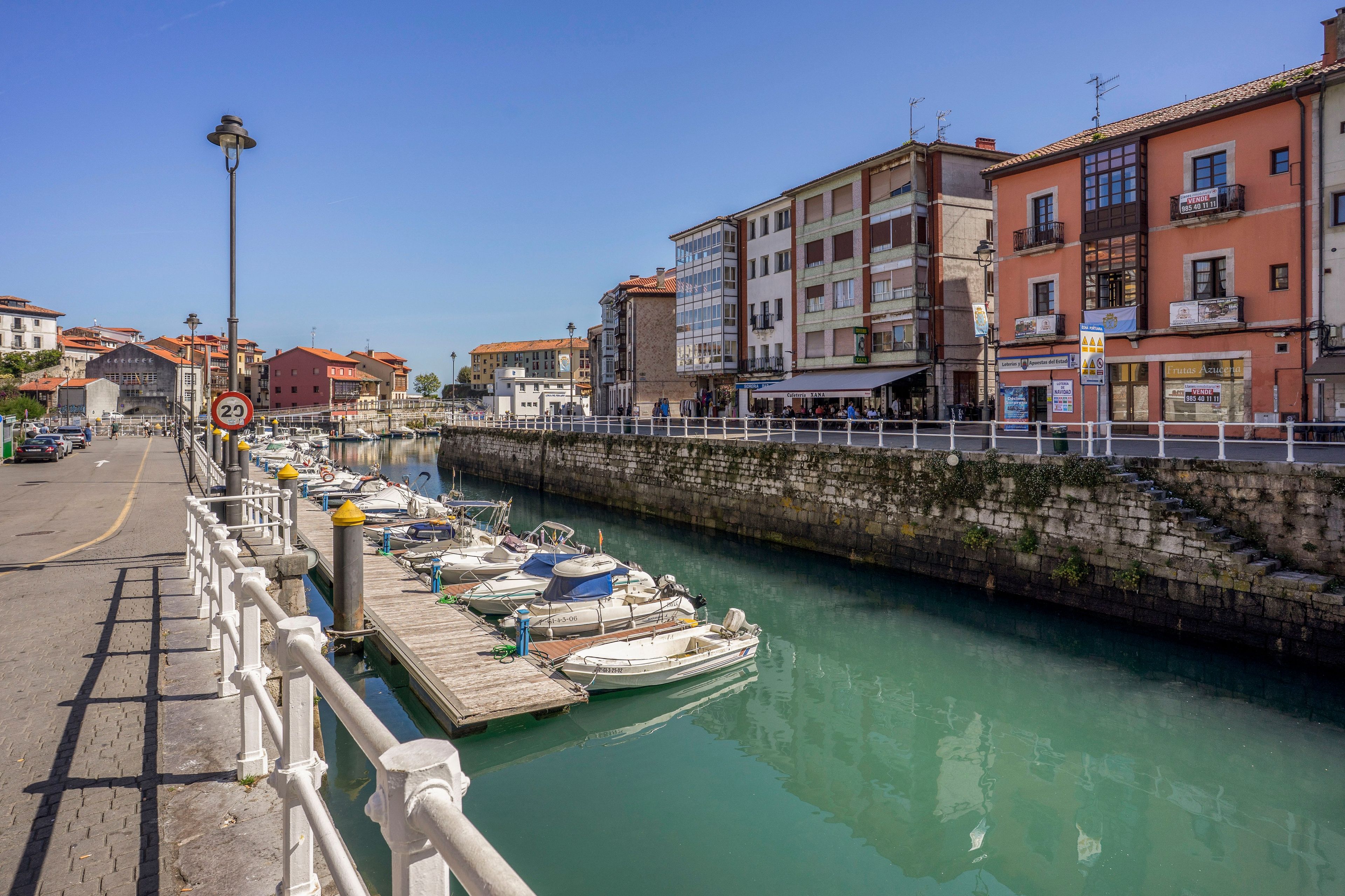 Un paseo marítimo con una hilera de barcos amarrados a lo largo del canal, junto a un muro de piedra y edificios con balcones.