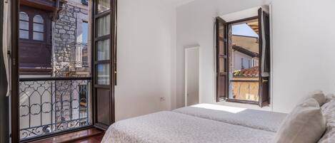 A bedroom with a bed, a window, and a view of a building outside.