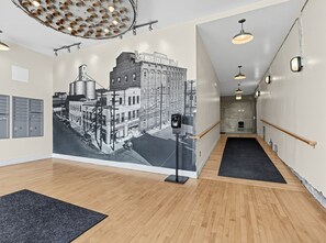 A hallway with a vintage street scene mural, wooden floors, and a security camera.