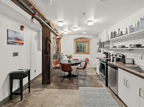 A modern kitchen with white cabinetry, a dining area with a round table and chairs, and a cityscape mural on the wall.