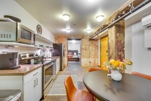 A compact kitchen with modern appliances, a dining area with a table and chairs, and a visible bed in the background.