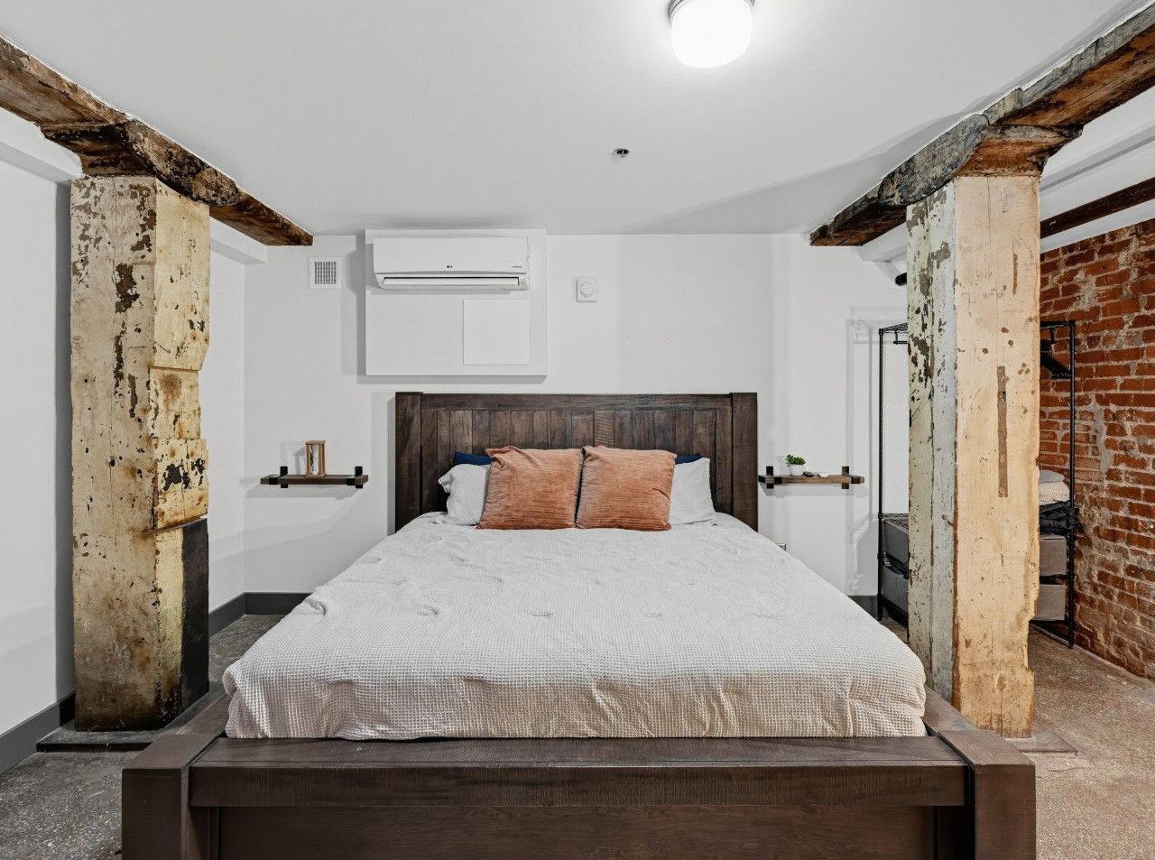 Une chambre avec un lit en bois, des murs blancs et un mur en briques apparentes.