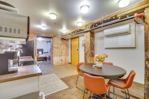 A compact hotel room with a kitchenette, a dining area with orange chairs, a round table, and a bed in the background.
