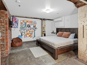 A bedroom with a bed, a bean bag, a wall mural, and a brick wall.