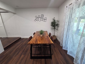 A dining area with a wooden table, chairs, a potted plant, and a wall-mounted artwork. - Delightful 2-bedroom house with AC in vibrant Miami (Miami)