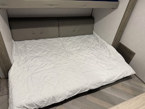 A bed with a quilted white cover, a headboard with buttons, and a wooden floor.