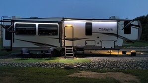 A large RV with a ladder, a covered area, and a name 'Wildwood Heritage Glider' on the side.
