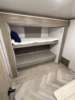 A bunk bed with a lower shelf, a door with a handle, and a herringbone-patterned floor. - Fabulous 3-bedroom RV with direct access to the Sebasticook River! (Benton)