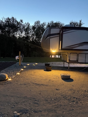 A stationary RV with a visible water spigot and a pot on the ground.