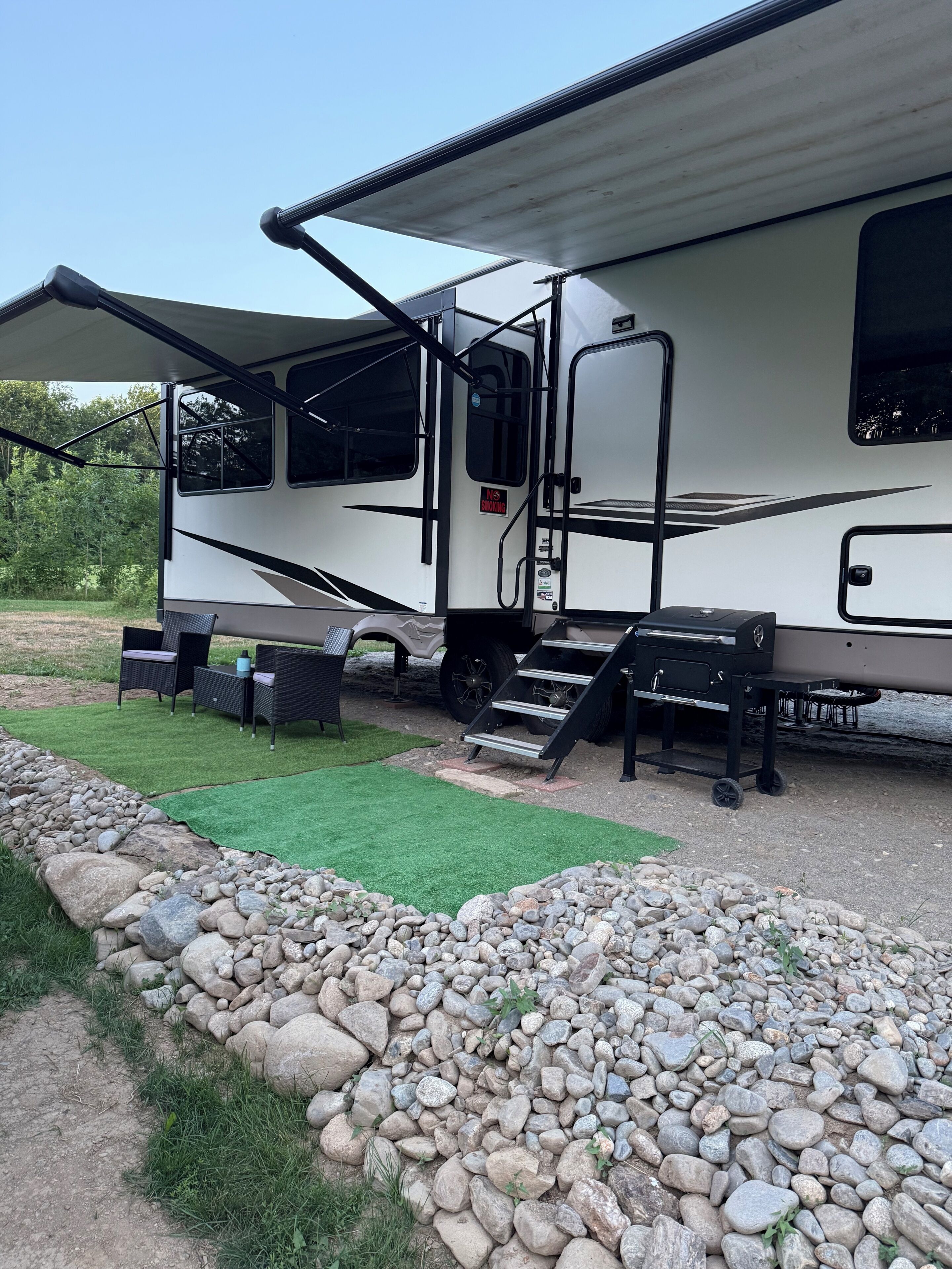 A recreational vehicle with an open door, a patio area with outdoor furniture, and a gravel path.