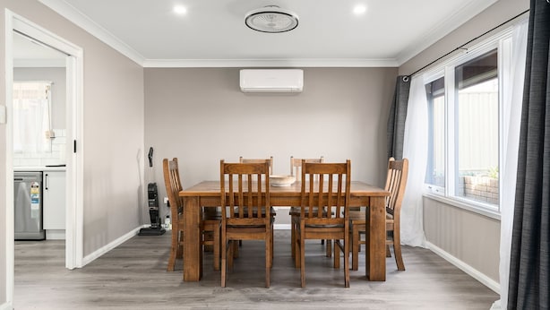 Un comedor con una mesa y sillas de madera, un ventilador de techo y una ventana con cortinas.