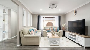 Una sala de estar moderna con un sofá, una mesa de centro, un televisor y un ventanal con cortinas.