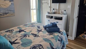 A bedroom with a bed, a desk, a TV, and a door.