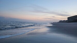 A beach with a calm sea, a sandy shore, and a building on the right.