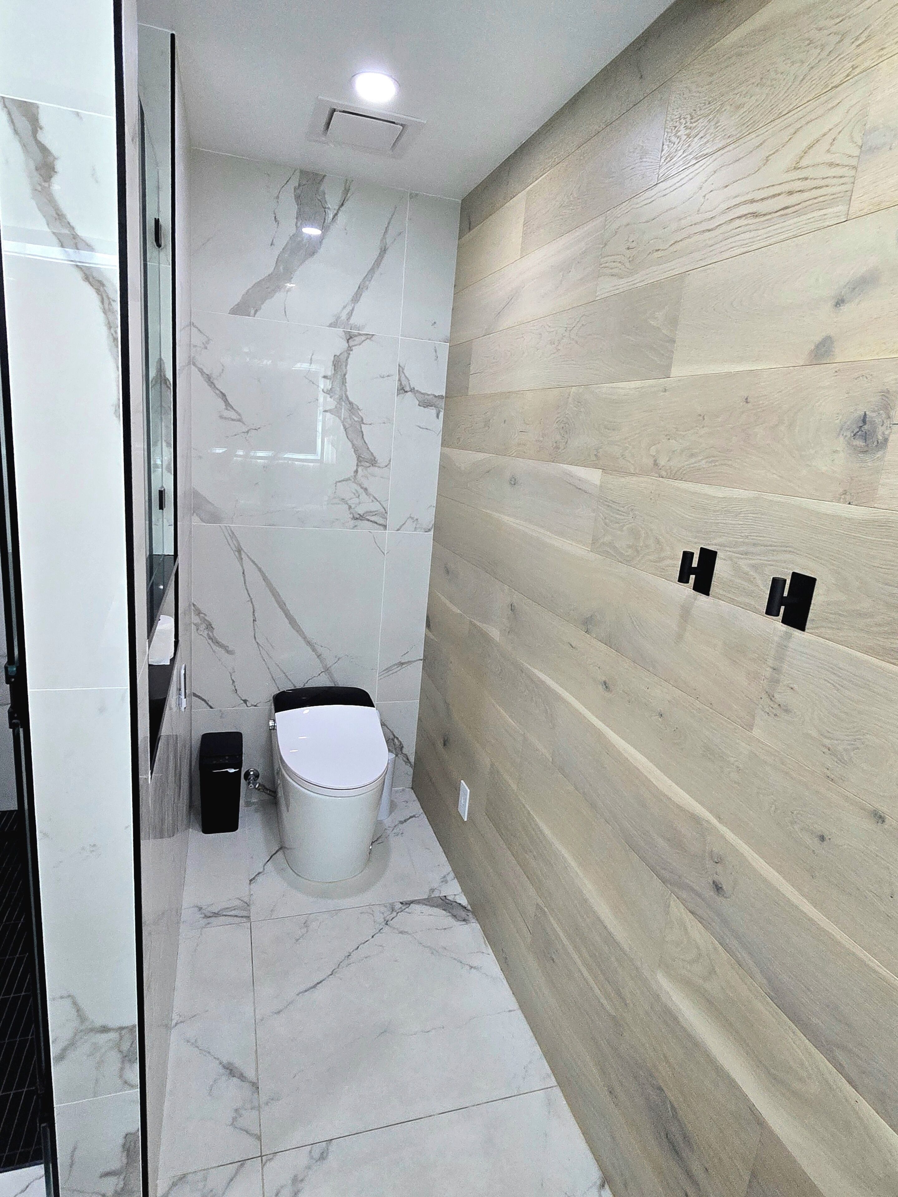 Un baño con inodoro, un cubo de basura y una pared de madera.