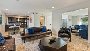 A modern living room with a leather sofa, a coffee table, and a dining area with blue chairs. - OSide Private PoolHome 4bed/3Bth (Oceanside)