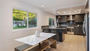 A modern kitchen with a central island, dark cabinetry, and a dining area with a white table and bench. - OSide Private PoolHome 4bed/3Bth (Oceanside)