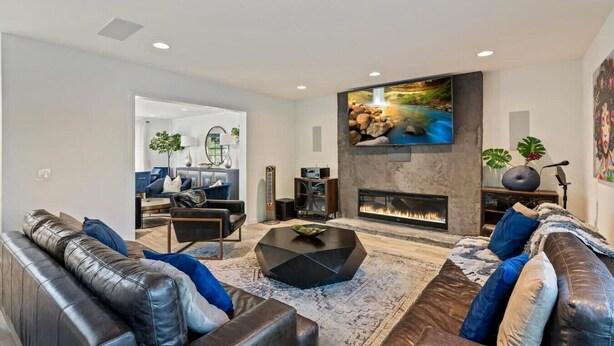 A modern living room with a fireplace, leather sofas, a coffee table, and a TV mounted on the wall. - OSide Private PoolHome 4bed/3Bth (Oceanside)