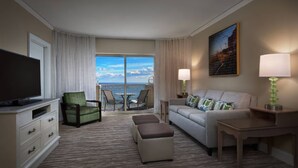 Ein Hotelzimmer mit Balkon, einem Flachbildfernseher, einer Couch, einem Sessel und einem Tisch mit Lampe.