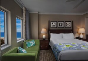 A hotel room with a bed, two bedside lamps, a green armchair, a window with a view of the ocean, and three framed pictures on the wall. - Ocean View -2 Bedroom-Marriott's OceanWatch Villas at Grande Dunes - Full Resort (Myrtle Beach)