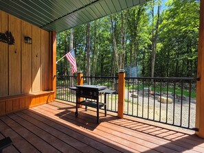 Un espacio al aire libre techado con una parrilla, una bandera y vistas a un bosque.