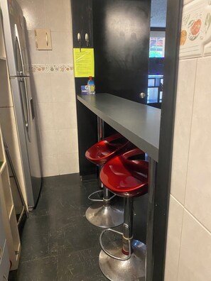 Eine schmale Küche mit Kühlschrank, Spüle und einer Bar mit roten Hocker.