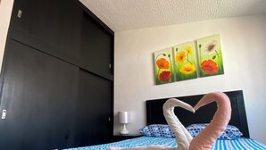 Hotellihuone, jossa on sänky, seinällä kukkakuva ja sängyllä joutsenen muotoinen pyyhe.