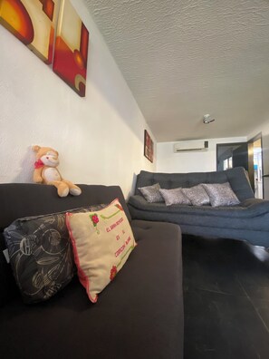 Ein Wohnzimmer mit einer dunklen Couch, einem Teddybären und einem Kissen mit Schrift.