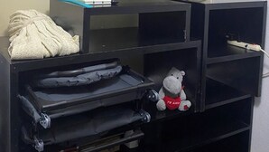 Television jalustalla, pehmeä pehmolelu ja taitettu viltti hyllyllä.