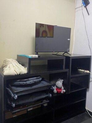 Ein Fernseher auf einem Schrank, ein Plüschtier und eine zusammengefaltete Decke auf einem Regal.