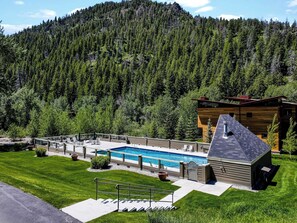Ein modernes Gebäude mit Schwimmbecken, umgeben von einem gepflegten Rasen und einer bewaldeten Berglandschaft.