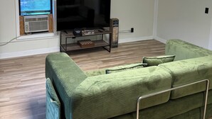 A living room with a green sofa, a flat-screen TV, and a window with blinds. - One bedroom apartment in the  finger lakes (Naples)