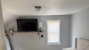 A bedroom with a bed, a television on a shelf, a window with blinds, and a ceiling light. - One bedroom apartment in the  finger lakes (Naples)