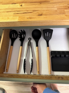 Un cajón con utensilios de cocina, incluyendo espátulas, pinzas y una taza medidora.