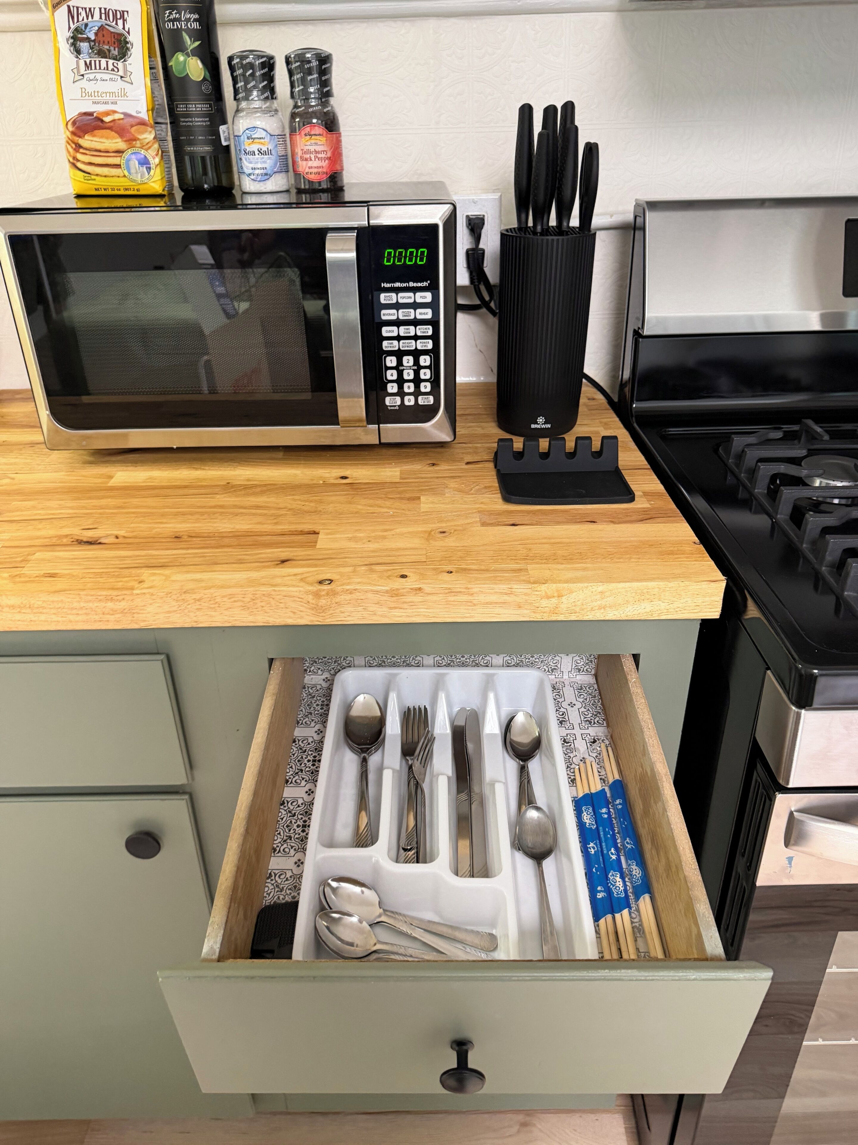 A kitchen with a microwave, stove, and drawer with utensils.