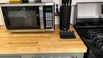 A kitchen with a microwave, stove, and drawer with utensils.