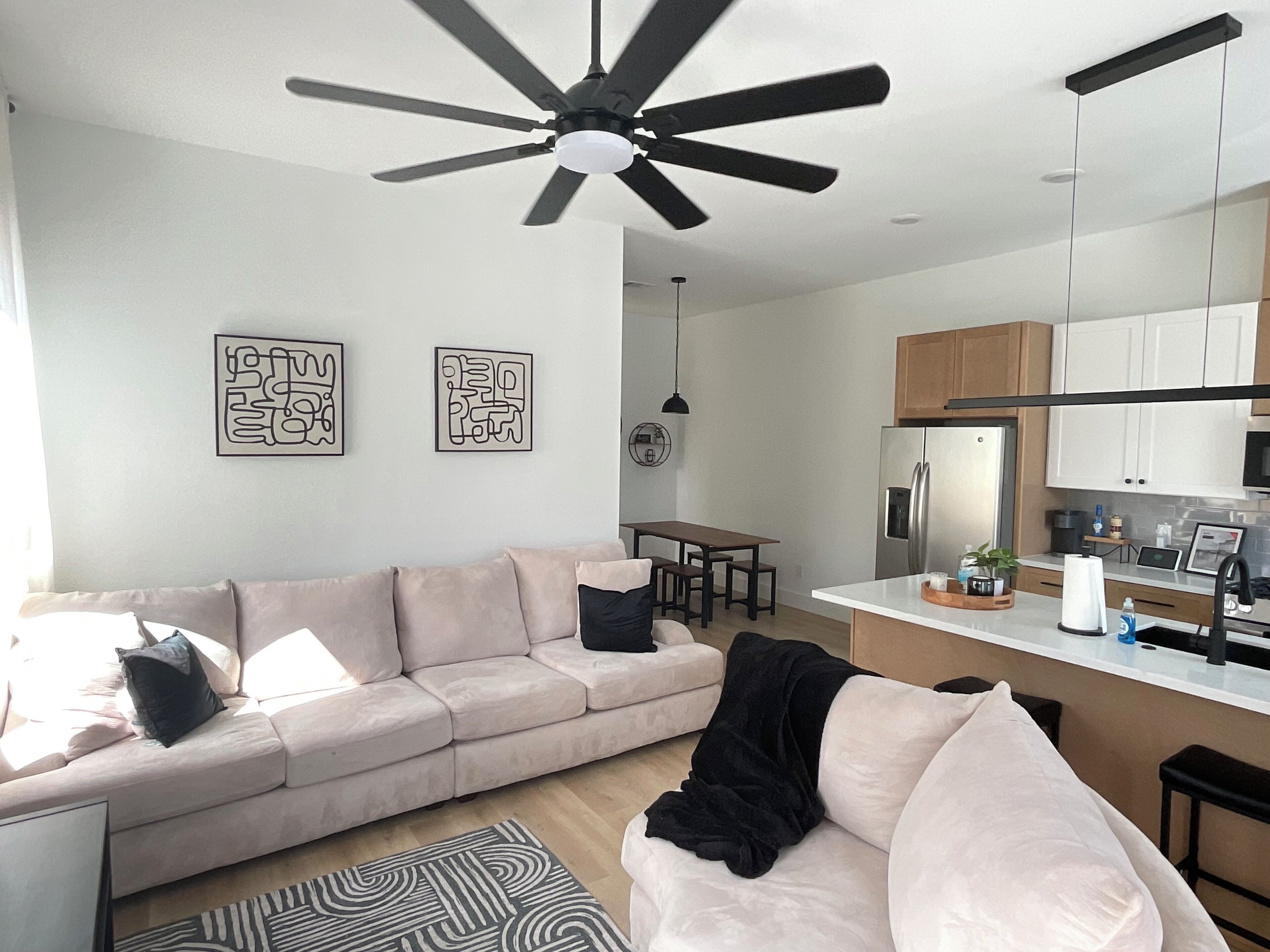 A modern living room with a beige sofa, a ceiling fan, and abstract wall art.