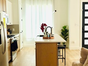 A modern kitchen with a central island, wooden cabinets, and a dining area with a chair.