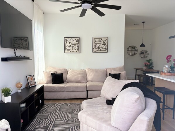 A living room with a beige sofa, a black ceiling fan, and abstract wall art.