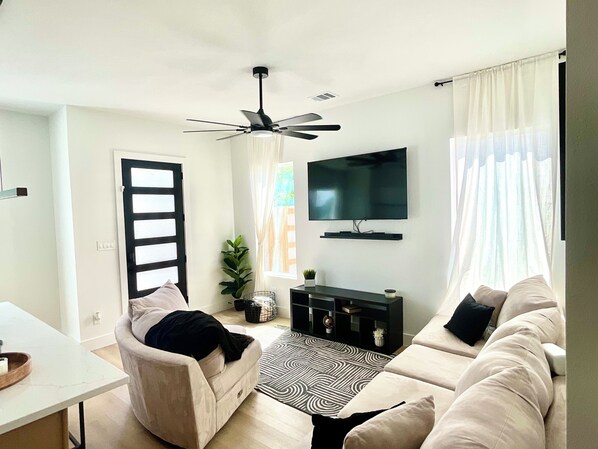 Ein Wohnzimmer mit einer Couch, einem Fernseher, einem Deckenventilator und einer Tür.