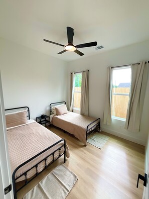 Ein Schlafzimmer mit zwei Betten, einem Deckenventilator und einem Fenster mit Vorhängen.