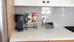 Una cocina con gabinetes blancos, una cafetera, un estante pequeño con condimentos y una tableta sobre la encimera.