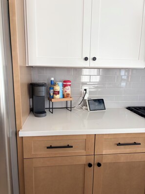 Eine Küche mit weißen Schränken, einer Kaffeemaschine, einer kleinen Ablage für Gewürze und einem Tablet auf der Arbeitsplatte.
