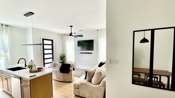 Una cocina moderna con una isla central, un comedor con mesa y sillas, un sofá y un televisor montado en la pared.