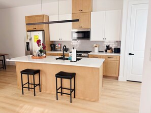 Eine moderne Küche mit Kochinsel, Holzschränken, Edelstahlgeräten und zwei schwarzen Barhocker.