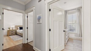 Ein Schlafzimmer mit Bett, Nachttisch, Lampe und einem Fenster mit Vorhängen.