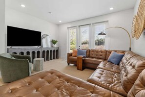 A modern living room with a leather sofa, a television, and a large window with blinds. - Lookout Living 1405–Downtown Access–Sleeps 8 (Chattanooga)