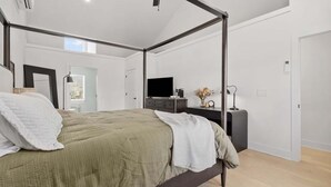 Un dormitorio moderno con cama con dosel, un televisor de pantalla plana, una mesita de noche y un escritorio pequeño con lámpara.